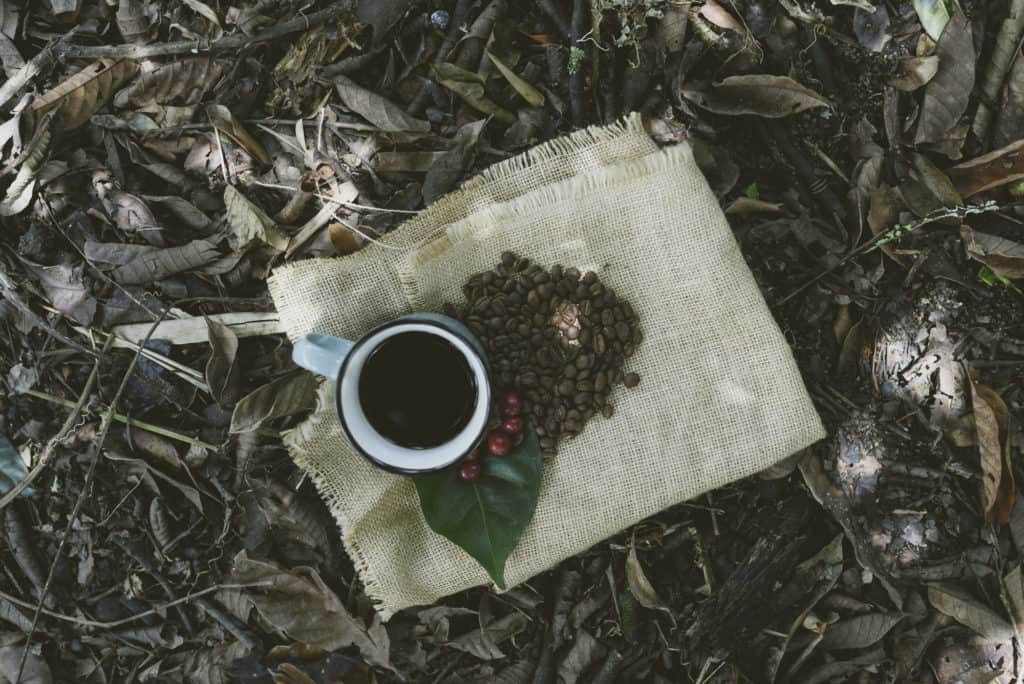 picture showing a burlap sack folded on the ground with a brewed cup of specialty colombian coffee and roasted coffee beans